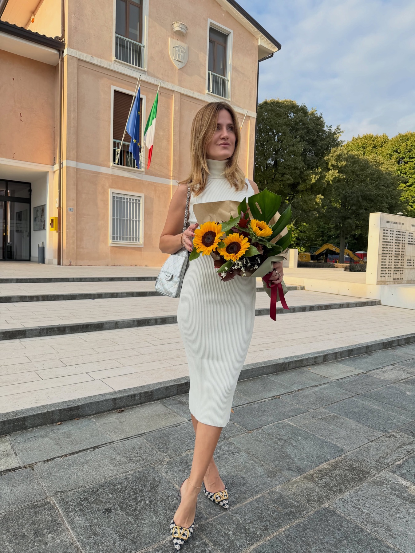 Valentina Morarasu in abito bianco davanti al Comune, con un mazzo di girasoli e le bandiere italiana ed europea sulla facciata