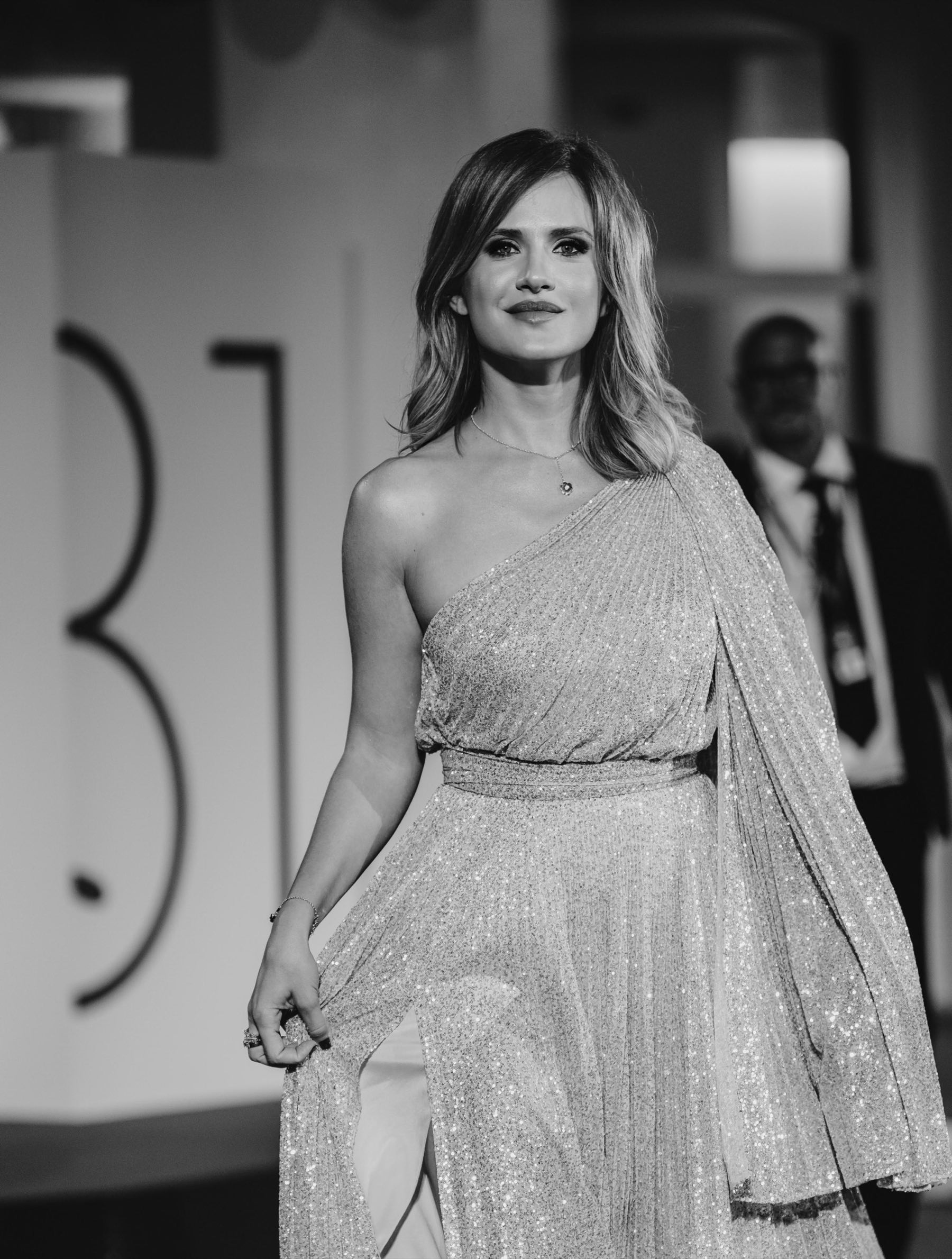 Ritratto in bianco e nero di Valentina Morarasu in abito plissé, davanti al logo dell'81ª Mostra del Cinema di Venezia